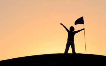 Person standing on a hill with their arms out and holding a flag